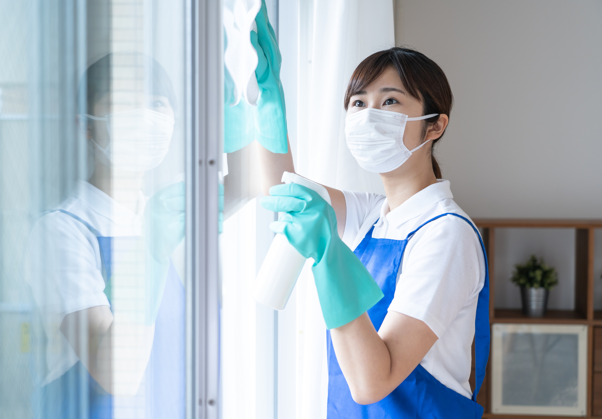 A woman in mask and gloves cleaning a window.